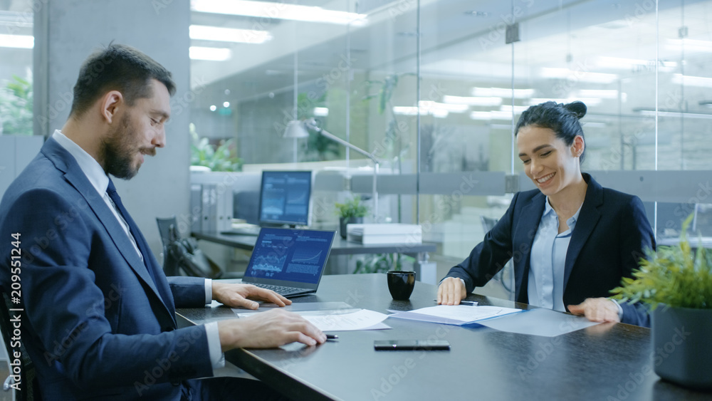 Fototapeta premium Businesswoman and Businessman Have Conversation. Draw up a Contract, Filling Papers in Conference Room. In the Background Modern Bright Office with Glass Walls.
