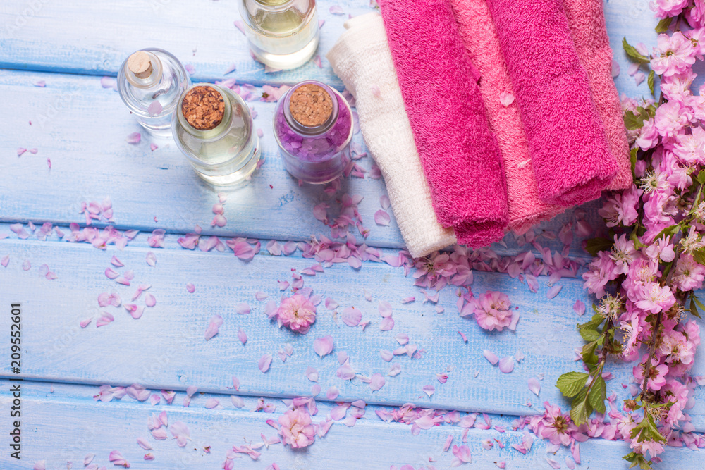 Essential aroma oil, flowers and pink towels on blue wooden background. Essential aroma oil, flowers and pink towels on blue wooden background.