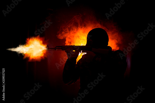 Silhouette of man with assault rifle ready to attack on dark toned foggy background or dangerous bandit in black wearing balaclava and holding gun in hand.