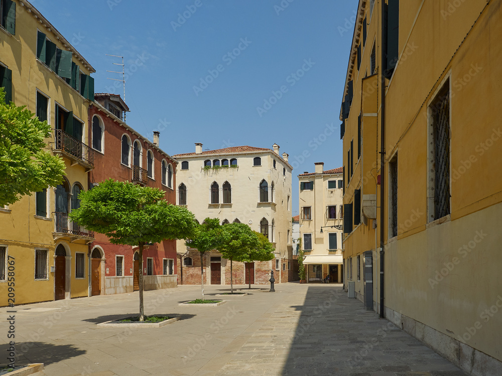 Square with green trees in Dorsoduro, Venice, Italy surrounded by historic colorful houses and apartments on a sunny day