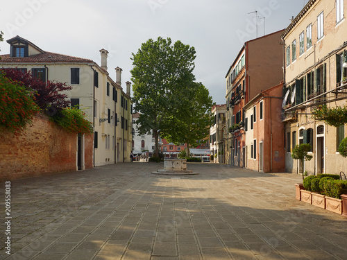 Open residential square with houses, ancient medieval well head and leafy green tree, Venice, Veneto, Italy