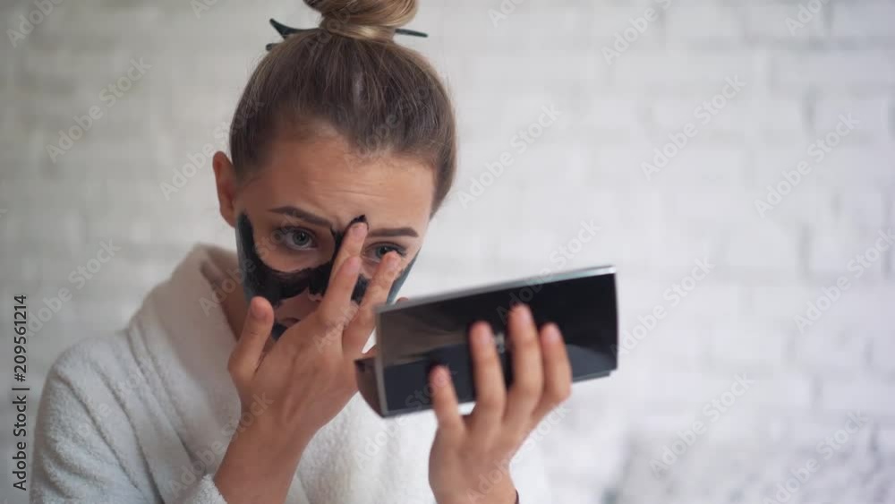Laughing young girl with a towel on her head puts a black mask on her face, day spa Laughing young girl with a towel on her head puts a black mask on her face, day spa