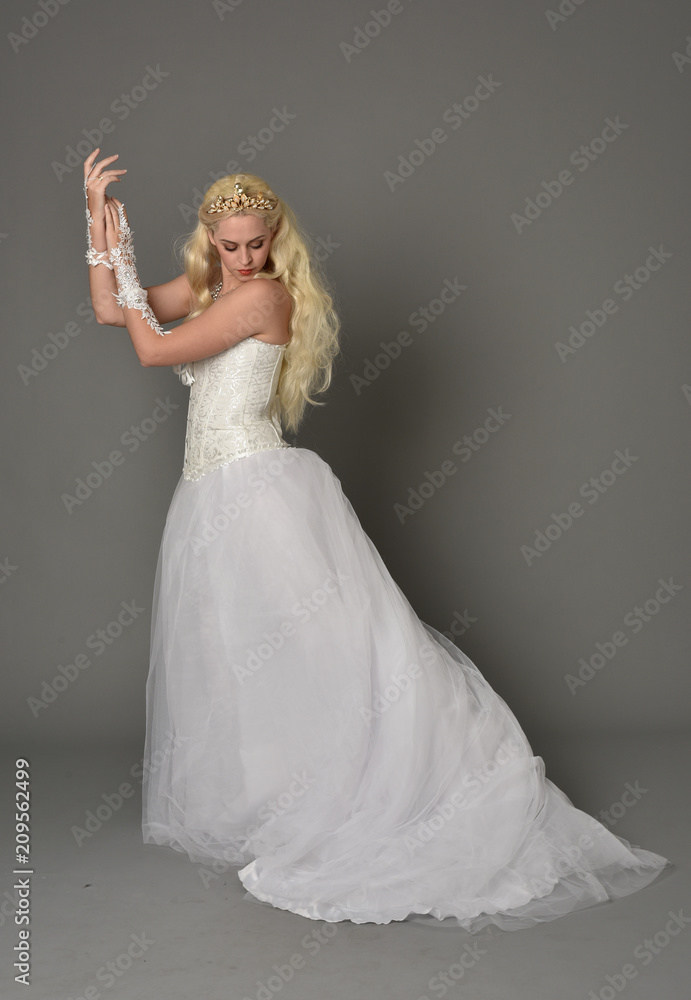 Naklejka premium full length portrait of blonde girl wearing white fantasy gown. standing pose in side profile, grey studio background.