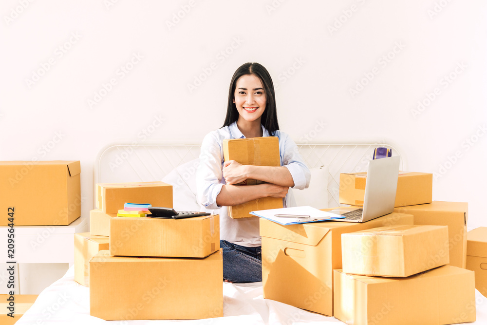 Young woman freelancer working and holding cardboard box on bed at home - SME business online and delivery concept Young woman freelancer working and holding cardboard box on bed at home - SME business online and delivery concept