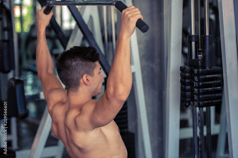 Portrait of young man doing exercise by using weight lifting equipment in sport gym, bodybuilder concept.