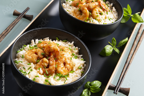 Two bowls of black color with rice and fried shrimp on a blue table. Asian food.