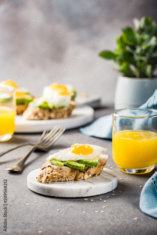 Healthy breakfast with open sandwich with fresh avocado and fried quail egg on small marble board on gray background. Copy space.
