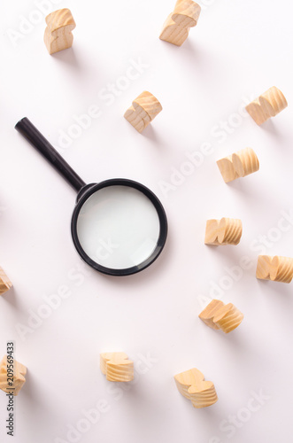 A magnifying glass lies in the center of the wooden figures of people who look at it. The concept of the search for workers and specialists, the search for a second half on a dating site. Headhunter.
