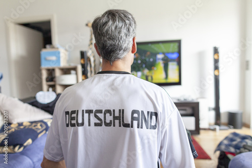 German fan sits in a Deutschland ( Germany ) jersey in front of a television