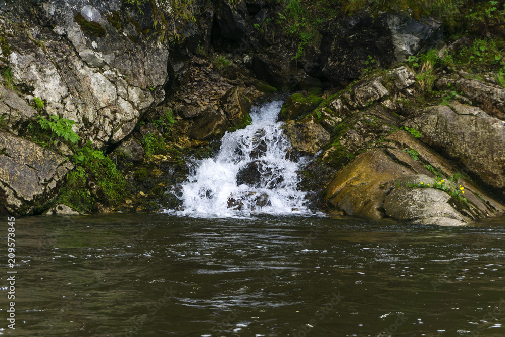 The spring follows a waterfall from the rock and flows into the river on a precipitous river bank The spring follows a waterfall from the rock and flows into the river on a precipitous river bank