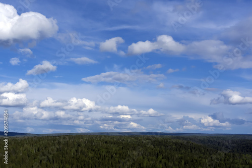 heavenly landscape - a blue sky with clouds over a wooded hilly land with a bird's eye view