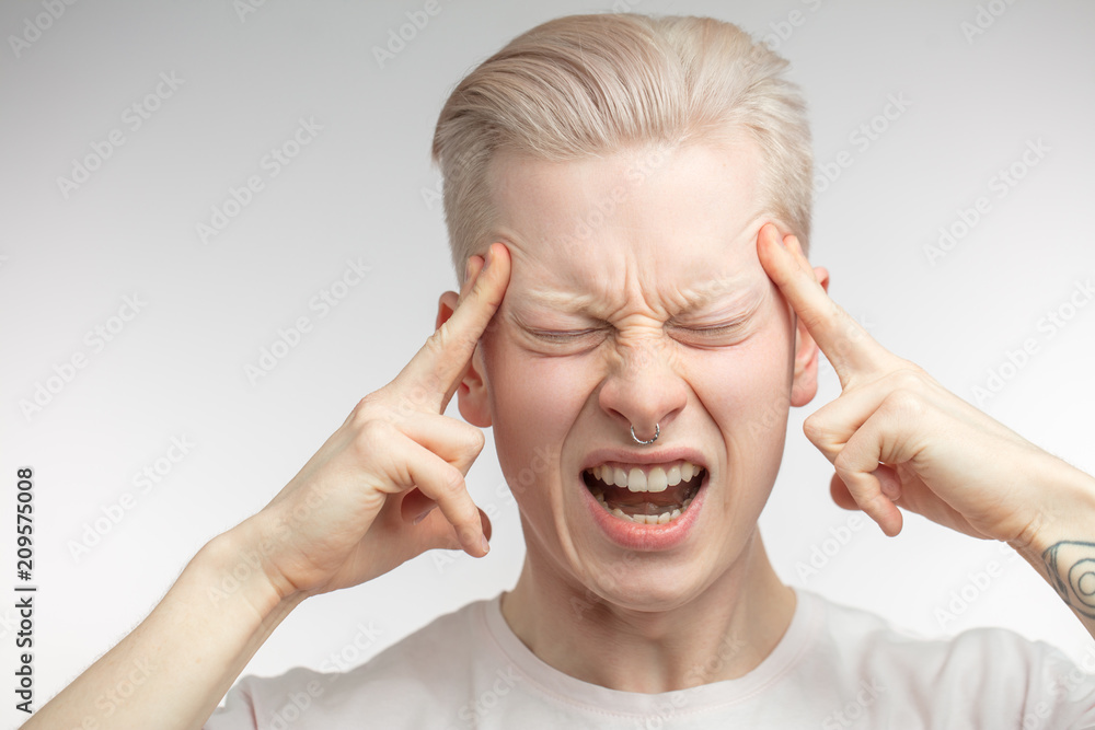 Close up face portrait of disappointed young blonde man keeping fingers on temples, as if asking to stop doing this, opens his mouth in silent scream. Close up face portrait of disappointed young blonde man keeping fingers on temples, as if asking to stop doing this, opens his mouth in silent scream.