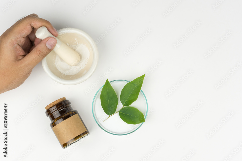 herbal medicine concept. pharmacist using a mortar and pestle, the organic green leaves in watch glass with a bottle on the white table in laboratory.