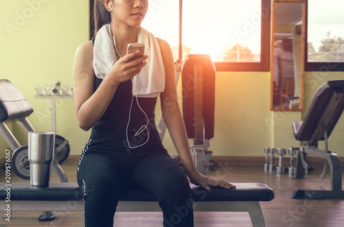 Fototapeta Naklejka Na Ścianę i Meble -  Female athletes listen to music using the phone while relaxi from exercise. Asian Athlete in Sports Apparel
