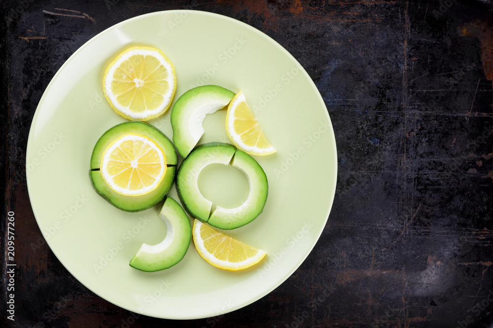 Sliced avocado and lemons on a green plate, avocado on a dark vintage background, vegetarian food, healthy natural food, tropical fruits for breakfast, copy space Sliced avocado and lemons on a green plate, avocado on a dark vintage background, vegetarian food, healthy natural food, tropical fruits for breakfast, copy space