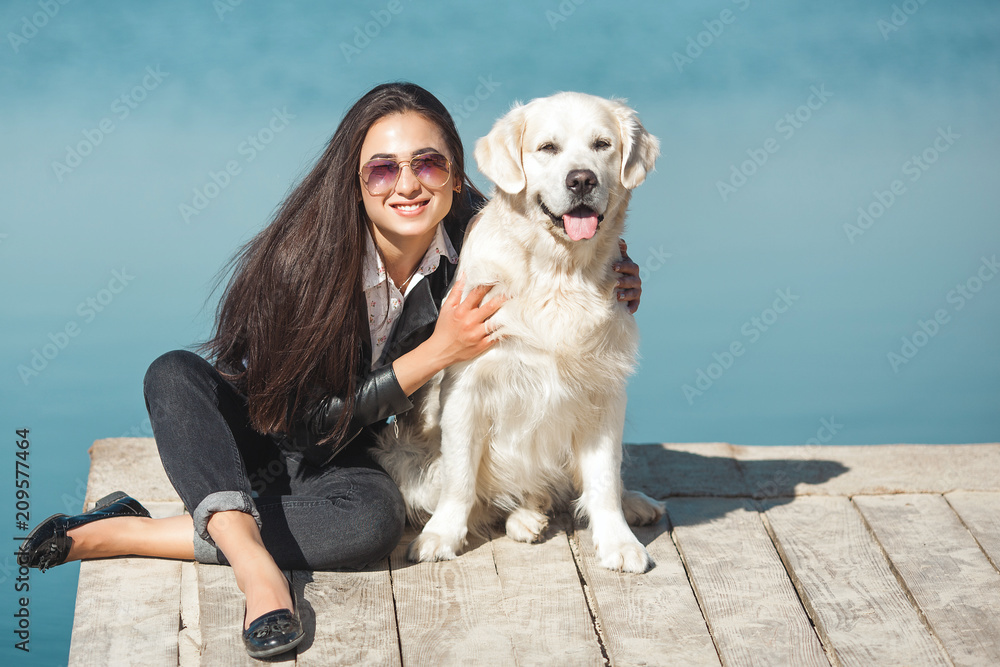 Young attractive woman sitting at the pier with her dog. Best friends outdoors Young attractive woman sitting at the pier with her dog. Best friends outdoors