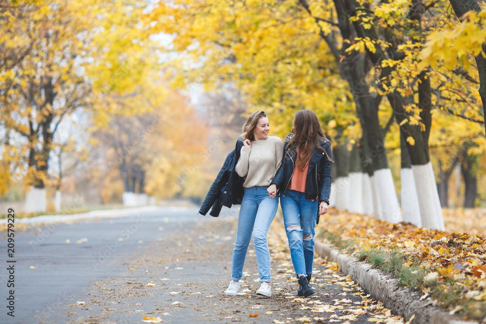 Fototapeta premium Young pretty girls having fun outdoors in autumn background. Cheerful friends in the fall time
