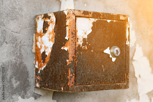 The old electric shield hangs on the exfoliating wall of the house, a rusty metal box hanging on the wall