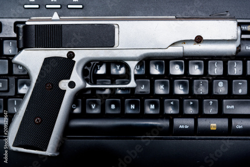 Gun laying on a computer keyboard, Crime or social network concept