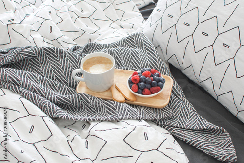 Breakfast bed Wooden tray Hotel room Early morning Concept interior Copy space Geometric sheet and pillow case Berries Cappuccino cup Biscuits Top view