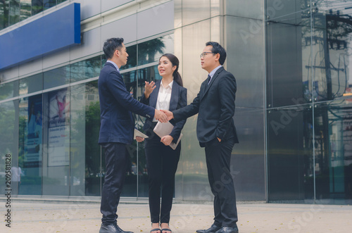 two attractive business man and a business woman meeting together and talking with discussion in business at outdoor in front of modern building office in city. business teamwork leadership concept.  © thithawat