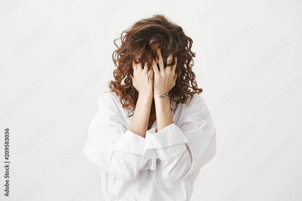 Studio portrait of tired or bothered woman hiding face in her curly hair and holding hands on it, expressing exhaustion or just being childish, standing over gray background. I am not seeing you Studio portrait of tired or bothered woman hiding face in her curly hair and holding hands on it, expressing exhaustion or just being childish, standing over gray background. I am not seeing you