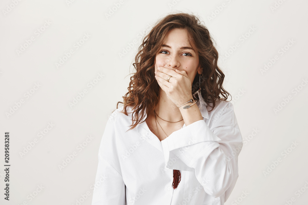 Emotive charming caucasian female covering mouth with hand while laughing over friend, standing over gray background. Girl can not stop chuckling over her awkward friend who asks classmate out Emotive charming caucasian female covering mouth with hand while laughing over friend, standing over gray background. Girl can not stop chuckling over her awkward friend who asks classmate out