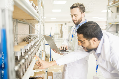 Multi-ethnic group of engineers wearing lab coats examining quality of measuring equipment while carrying out inspection at warehouse of modern factory