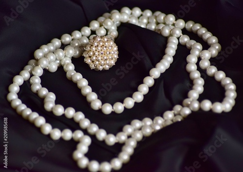 Ring and necklace of white pearls lie on black fabric.