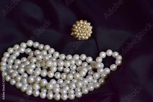 Ring and necklace of white pearls lie on black fabric.