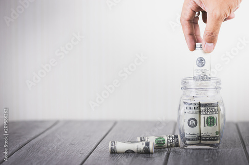 Businessman hand putting money hundred dollars in glass bottle  Concept of saving money  Business investment financial plan  Sustainable growth and stability in the future  With copy space