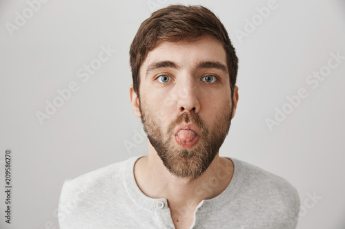 That is what I think about your idea. Portrait of funny calm guy with beard, being bothered or childish while standing over gray background and sticking out tongue. Trying to annoy girlfriend