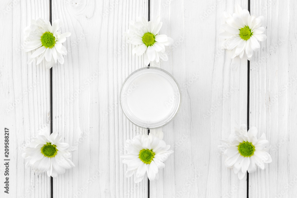 Obraz premium Chamomile cream. Face and body care. Cosmetics in small jar near chamomile flowers on white wooden background top view pattern