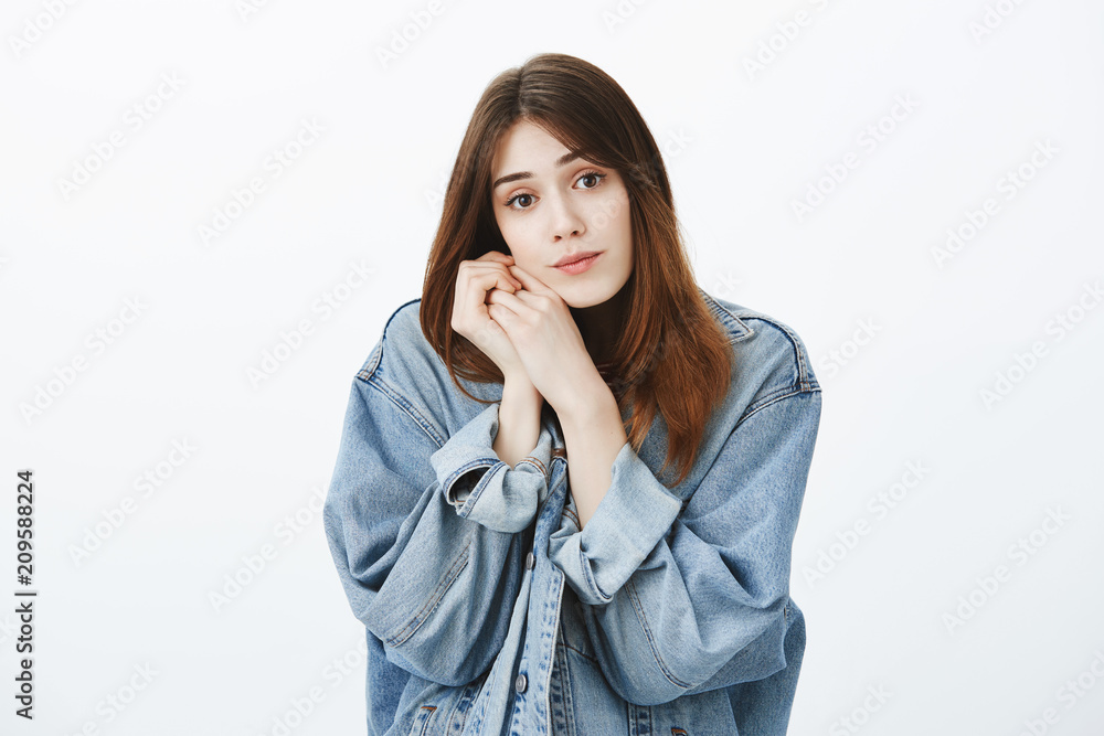 Studio shot of begging cute european girl in denim jacket, leaning head on hands and gazing at camera with angel look, wanting something, making impression on boyfriend over gray background Studio shot of begging cute european girl in denim jacket, leaning head on hands and gazing at camera with angel look, wanting something, making impression on boyfriend over gray background