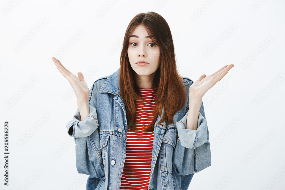 No clue what is happening. Studio portrait of questioned unaware attractive girl with brown hair in stylish denim jacket, raising spread palms and shrugging with clueless expression, having no idea No clue what is happening. Studio portrait of questioned unaware attractive girl with brown hair in stylish denim jacket, raising spread palms and shrugging with clueless expression, having no idea
