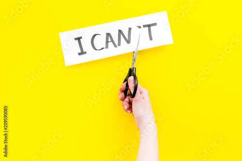 I can concept. Motivate youself, believe in yourself. Hand cut off the letter t of written word I can't by sciccors. Yellow background top view copy space