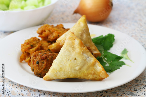 Plate full of Indian samosas, pakoras and onion rings with fresh coriander leaves on the side
