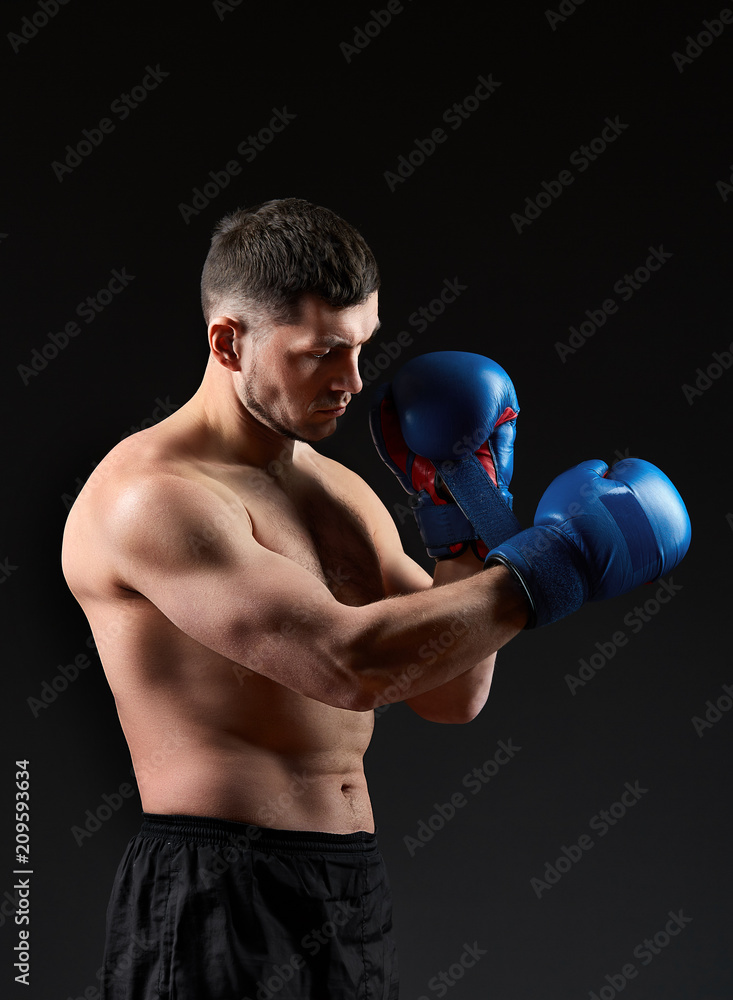Low key studio portrait of handsome muscular fighter practicing boxing on dark blurred background