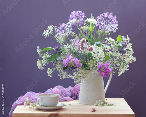 Still life with garden and wild flowers in a jug and a tea pair on a table