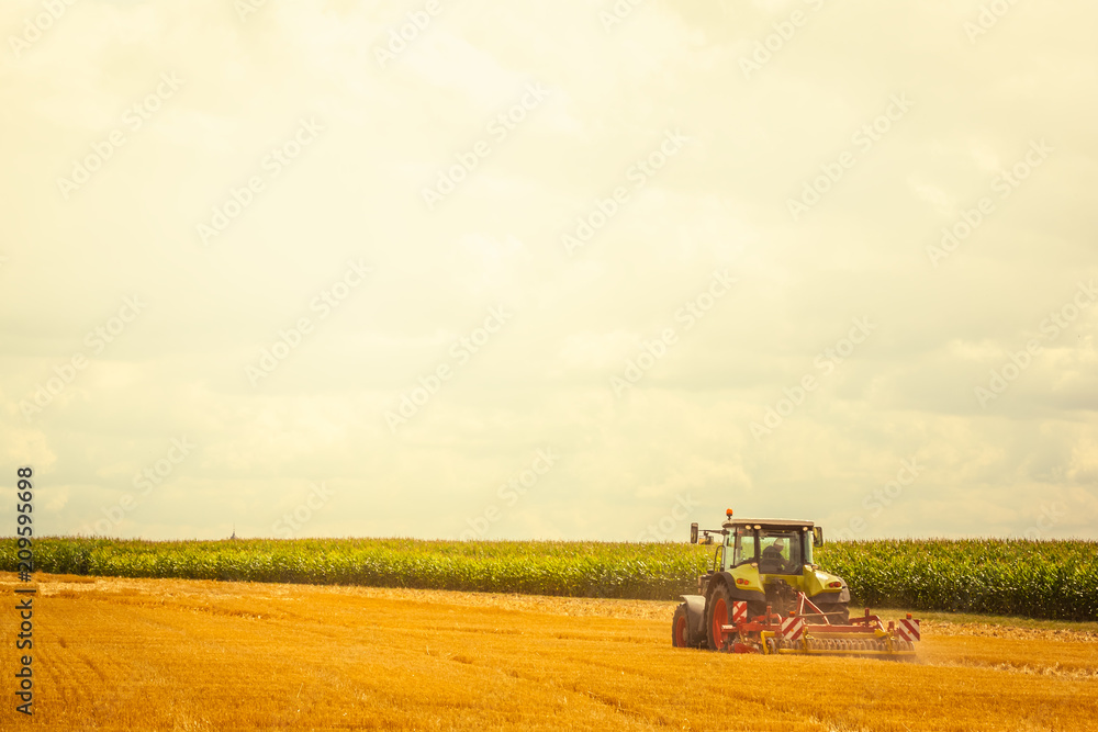 Fototapeta premium Agriculture - green tractor ploughing at the field on a sunny day