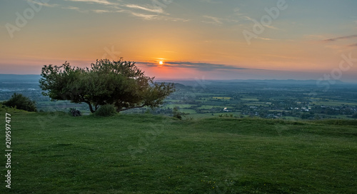 View of sunset from Crickley hill Gloucestershire with  a tree on the edge of the hillside in the foreground. photo