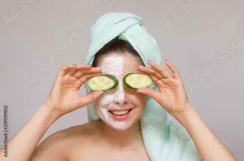 Woman with cucumber slice and with face cream over her face. Face skin treatment concept.