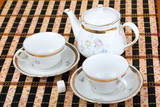 Two empty white porcelain cup and teapot on the table covered with striped bamboo table mat