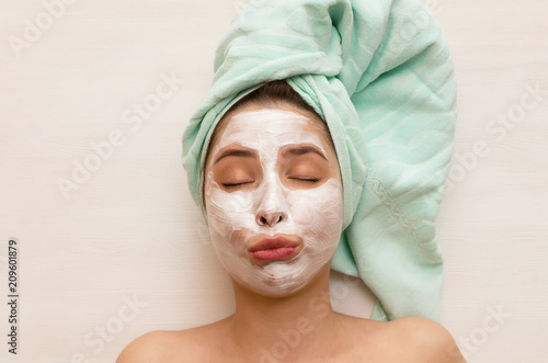 Woman laying on the beautician table in a salon with sour cream over her face. Face skin care concept.