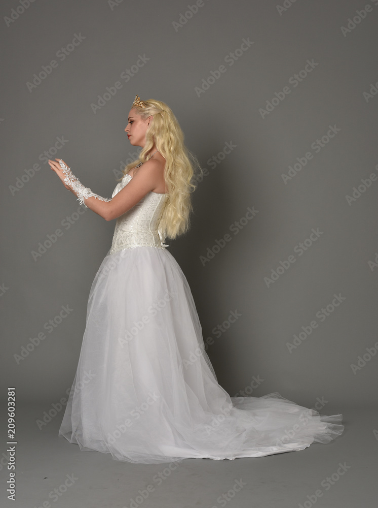full length portrait of blonde girl wearing white fantasy gown. standing pose in side profile, grey studio background. full length portrait of blonde girl wearing white fantasy gown. standing pose in side profile, grey studio background.