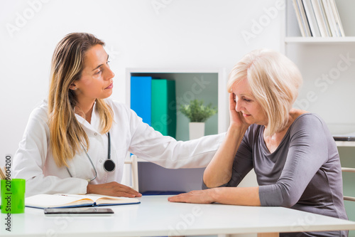 Female doctor consoling  her senior patient in office.