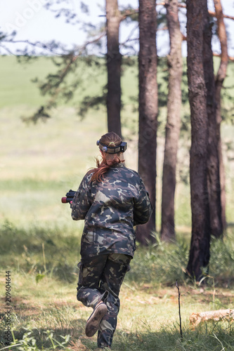 Girl in camouflage with a gun, plays laser tag in the forest. the player is aiming. Lasertag shooting game in open air. Military sport. Simulation of military operations