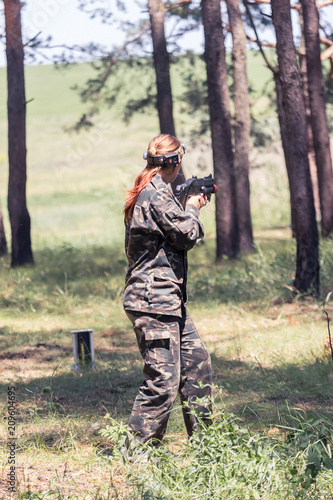 Girl in camouflage with a gun, plays laser tag in the forest. the player is aiming. Lasertag shooting game in open air. Military sport. Simulation of military operations