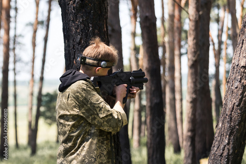 Young boy in camouflage with a gun, plays laser tag in the forest. the guy is aiming. Lasertag shooting game in open air. Military sport. Simulation of military operations