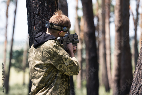 Young boy in camouflage with a gun, plays laser tag in the forest. the guy is aiming. Lasertag shooting game in open air. Military sport. Simulation of military operations